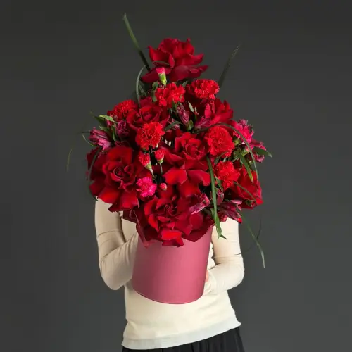 Цветочная композиция из красных гвоздик и роз с берграссом в шляпной коробке